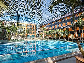Außenansicht Hotel Victory, Therme Erding - davor ein großes Schwimmbecken der Therme und Palmen